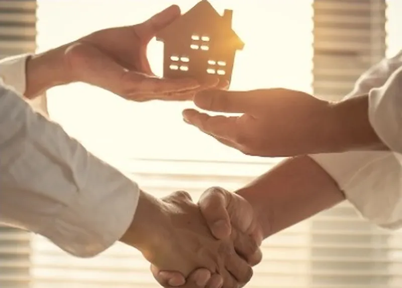 Handshake as a small wooden house is handed over